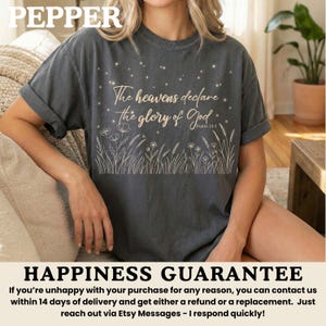 A woman wearing a pepper gray t-shirt with a gold starry night and wildflower print, sitting on a light-colored sofa.