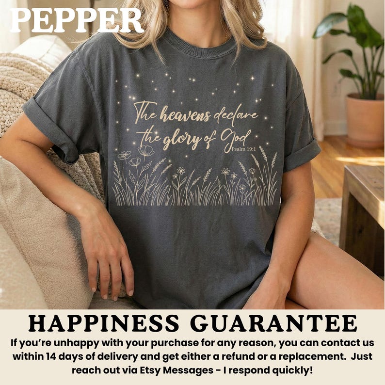 A woman wearing a pepper gray t-shirt with a gold starry night and wildflower print, sitting on a light-colored sofa.
