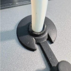 May include: A close-up shot of a black stylus holder with a white stylus. The holder has a circular base with a curved opening to hold the stylus. The holder is made of plastic and has a matte finish. The stylus is white and cylindrical.