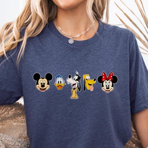 May include: Heather navy blue t-shirt featuring a line of cartoon character faces: Mickey Mouse, Donald Duck, Goofy, Pluto, and Minnie Mouse. The shirt has short sleeves and a crew neck. The words "Heather Navy" are printed on a small label.