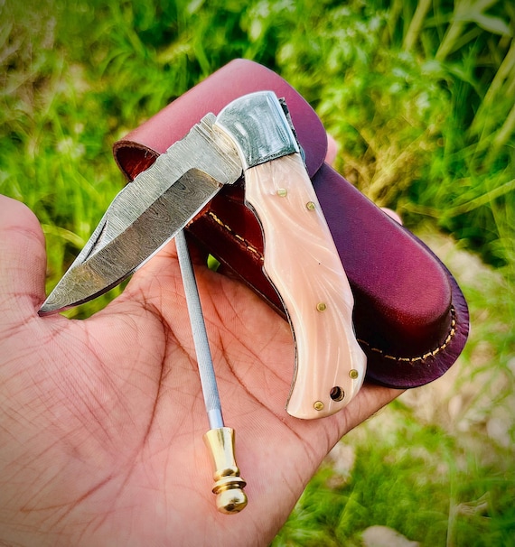 A hand-forged Damascus steel folding knife with a custom engraving and leather sheath — the kind of heirloom gift a guy will pass down to his kids.