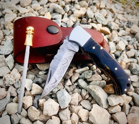 Handmade Damascus steel folding knife with a leather pouch — the layered-steel pattern alone makes it visually striking, and custom engraving elevates it to heirloom territory.