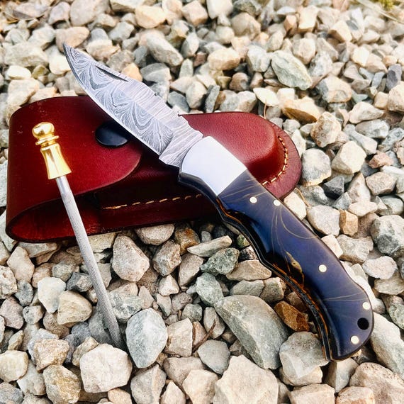 Handmade Damascus steel folding knife with a leather pouch — the layered-steel pattern alone makes it visually striking, and custom engraving elevates it to heirloom territory.