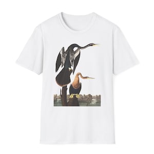Könnte beinhalten: Weißes T-Shirt mit einer detaillierten Illustration von zwei Anhinga-Vögeln, die auf einem Baumstamm sitzen. Die Vögel haben dunkles Gefieder, lange Hälse und gelbe Schnäbel. Das Design beinhaltet einen Landschaftshintergrund.