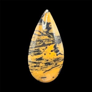 May include: A teardrop-shaped gemstone with a polished surface. The stone features a vibrant yellow base color, overlaid with striking black, linear patterns. The gemstone is set against a black background, highlighting its natural beauty.