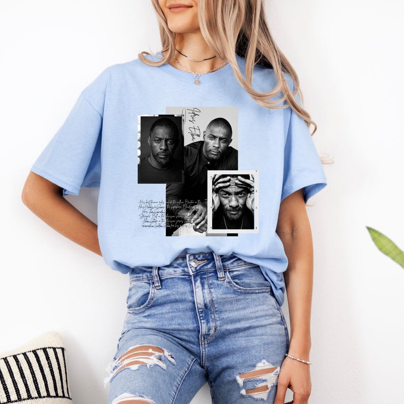 May include: Light blue t-shirt featuring a collage of three black and white portraits. The portraits are of a man, with the name "Idris Elba" written in cursive. The shirt also has script writing.