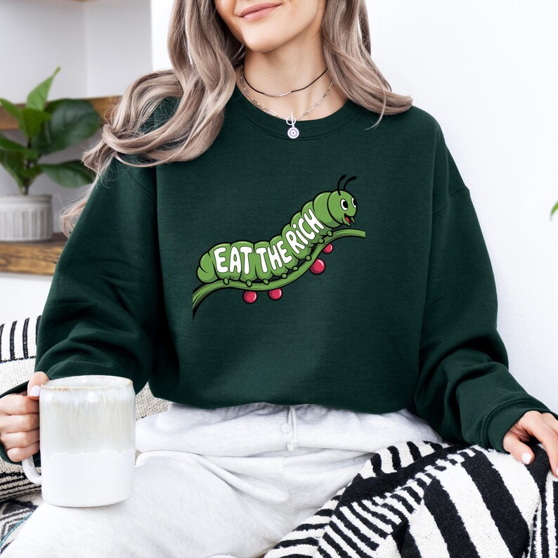 Puede incluir: Sudadera verde oscuro con un dise&ntilde;o de oruga de dibujos animados. La oruga verde est&aacute; sobre una rama con bayas rojas, y el texto "EAT THE RICH" se muestra en verde y blanco. La sudadera es de color verde oscuro liso.