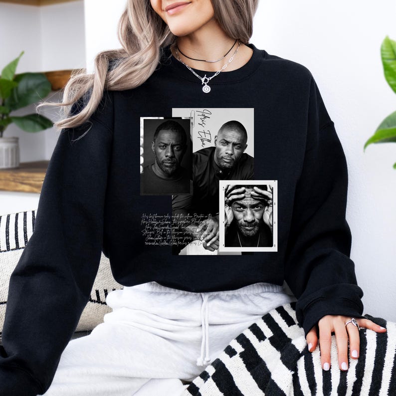 May include: Black sweatshirt featuring three black and white portraits of a man. The portraits are arranged in a collage with the name "Idris Elba" and script text. The sweatshirt is worn by a person.