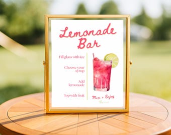May include: A framed sign with the words "Lemonade Bar" in pink script. The sign includes instructions for making lemonade and a watercolor illustration of a pink lemonade drink with a lime slice. The frame is gold.