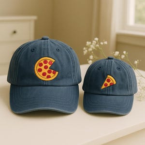 May include: Two blue baseball caps with pizza slice designs. One cap features a pizza slice, and the other has a pizza slice design. The caps are made of a soft material and have a curved brim. The caps are a fun and casual accessory.