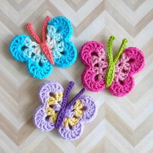Può includere: Tre applicazioni a farfalla all'uncinetto nei toni del blu, rosa e viola. Ogni farfalla ha una diversa combinazione di colori, con dettagli come le antenne e il centro delle ali in colori contrastanti. Le farfalle sono fatte a mano.