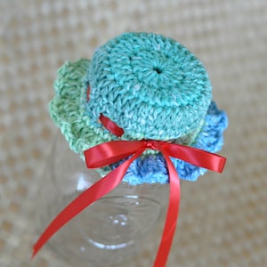 May include: A crocheted jar lid with a blue, green, and white design. A red ribbon is tied around the lid with a bow.