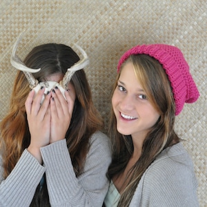May include: Two women, one wearing a pink knitted beanie and the other with a pair of antlers covering her face, are smiling at the camera.