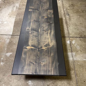 May include: A rectangular wooden table with a dark stained top and black metal trim. The wood grain is visible, with a mix of dark and light brown tones. The table's dimensions are not visible in the image.