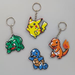 May include: Four colourful pixelated Pokemon keychains: a green Bulbasaur, a yellow Pikachu, a blue Squirtle, and an orange Charmander.