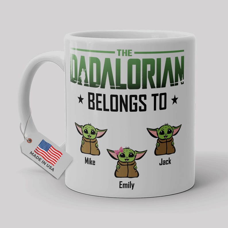 May include: A white ceramic mug featuring the green text THE DADALORIAN BELONGS TO above three cartoon green creatures in brown robes. The names Mike, Emily, and Jack are printed below each character. A small tag with a US flag is attached.
