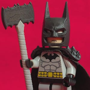 Puede incluir: Una figura de Lego de Batman con una capucha y capa negras, un traje gris y negro, sosteniendo un hacha gris. El fondo es rojo liso.