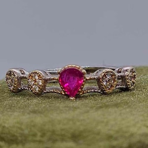Peut inclure: Bague en argent et or ornée d'une pierre précieuse rose vif en forme de poire au centre. La bague présente un design délicat avec de petits accents ronds de chaque côté de la pierre centrale, créant un bijou élégant et attrayant.