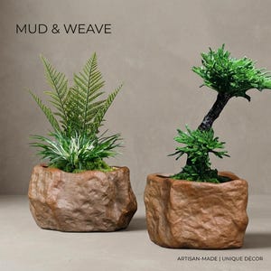 May include: Two brown, rock-textured planters containing green plants. The left planter holds a fern-like plant, while the right holds a small, tree-like plant. Text reads MUD & WEAVE and ARTISAN-MADE | UNIQUE DÉCOR.