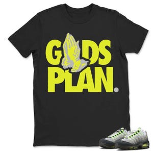 May include: Black t-shirt with the words "GOD'S PLAN" in bright yellow, featuring a praying hands graphic. A pair of gray and neon green sneakers are at the bottom right.