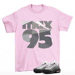 May include: A light pink t-shirt with the text "max 95" in a gray and white geometric design. Below the shirt are a pair of gray and white sneakers with black soles and pink accents.