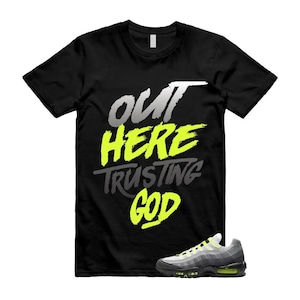 May include: Black t-shirt with the text "OUT HERE TRUSTING GOD" in white, yellow, and grey. A pair of grey, black, and yellow athletic shoes are in the lower right corner.