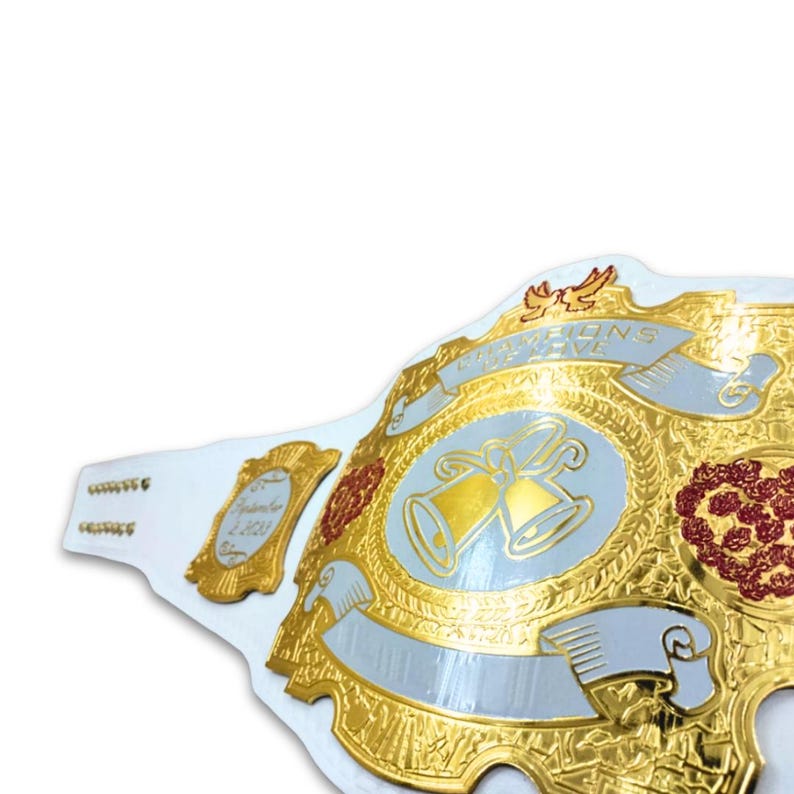 May include: White wedding championship belt with gold accents and red and white flowers. The belt features two silver bells and the words "Champions of Love".