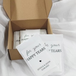 May include: A brown cardboard box filled with white packets. Each packet has the text "for your HAPPY TEARS" in black script, a small black heart, and the names "JESSICA & JASON" with the date "12.06.2025".