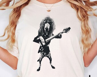 May include: Ivory-colored t-shirt featuring a black and white illustration of a dog playing an electric guitar. The dog has long hair and is wearing a black outfit. The word "Ivory" is printed in black on the bottom right.