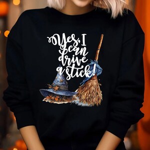 May include: Black sweatshirt with the text "Yes, I can drive a stick!" in white script. The graphic includes a witch's hat with autumn leaves and a broom. The design is perfect for Halloween or a witch-themed event.