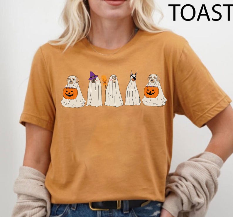 May include: Mustard-colored t-shirt featuring a Halloween-themed graphic. The graphic depicts five dogs dressed as ghosts, with one holding a jack-o'-lantern. The word "TOAST" is printed in black at the top right corner.