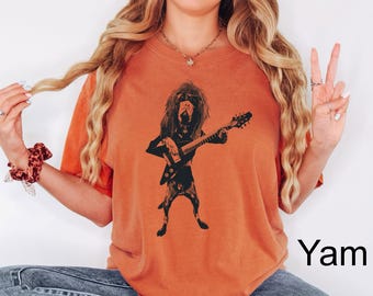 May include: Orange t-shirt featuring a black graphic of a dog playing an electric guitar. The dog has long hair and is in a rock and roll pose. The shirt is a solid color and has short sleeves.
