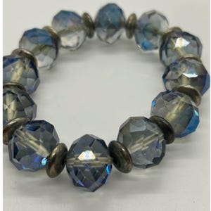 Peut inclure: Un bracelet circulaire composé de perles en verre facettées bleu-gris translucides alternant avec de petits disques d'espacement métalliques de couleur argentée. Les perles présentent une surface réfléchissante à facettes multiples.