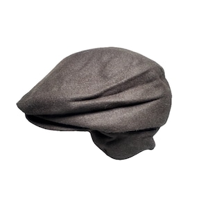 Puede incluir: Gorra newsboy marrón de lana. El sombrero tiene una corona redondeada y una visera pequeña y rígida. La gorra está hecha de una tela suave y texturizada en un color liso y neutro. Un estilo clásico adecuado para diversas ocasiones.