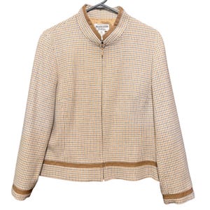 Puede incluir: Una chaqueta de color beige y azul claro con estampado de pata de gallo, cuello alzado y cremallera frontal completa. La chaqueta presenta un ribete de aspecto de cuero color canela en el cuello, los puños y el dobladillo. Etiqueta Pendleton visible.