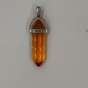May include: A pendant featuring a translucent, amber-colored, hexagonal crystal point encased in a silver-toned metal cap with a circular bail at the top. The crystal has a smooth, polished surface and a pointed tip, suspended by the metal hardware.