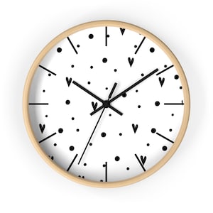 May include: Round wall clock with a light wood frame. The white face features black dots, hearts, and lines. Black hands indicate the time. A decorative piece for any room.