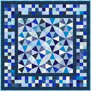 May include: A square quilt featuring a central panel of blue, navy, and light blue triangles arranged in pinwheel patterns. The center is framed by a dark navy border, surrounded by an outer border of small, multi-patterned blue and white squares.