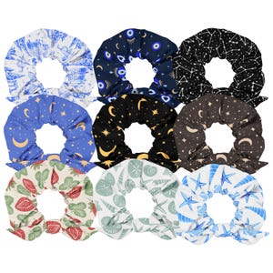 May include: Nine fabric scrunchies in various patterns. Designs include a blue and white Eiffel Tower print, a navy blue evil eye print, a black constellation print, a blue crescent moon print, a black crescent moon and star print, a brown crescent moon and star print, a red and green leaf print, a white seashell print, and a blue starfish print.