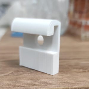 May include: White plastic clip with a rounded top and a hole in the center. The clip is designed to hold items in place.