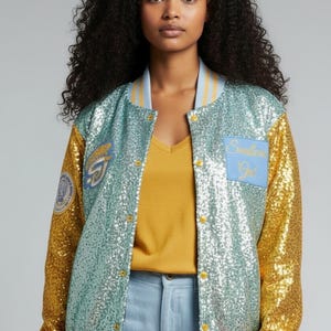 May include: A sequined bomber jacket with a teal body and gold sleeves. The jacket features a light blue collar and cuffs with yellow stripes. Patches with text are visible on the jacket.