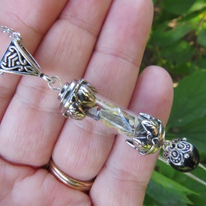 May include: A silver chain necklace with a glass vial pendant filled with crystals and a black onyx bead. The vial is adorned with silver filigree.