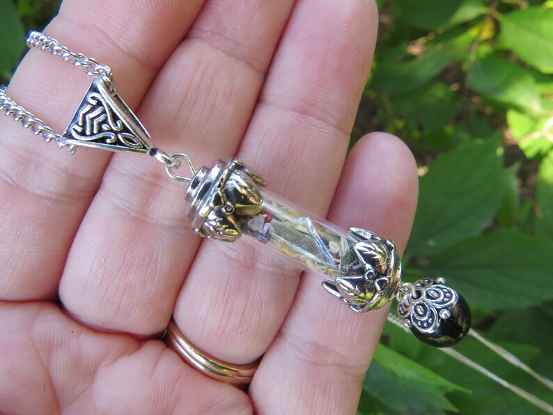 May include: A silver chain necklace with a glass vial pendant filled with crystals and a black onyx bead. The vial is adorned with silver filigree.
