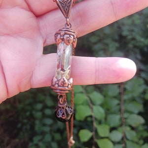 May include: A copper necklace with a long, clear glass pendant filled with dried herbs and a black bead at the bottom.