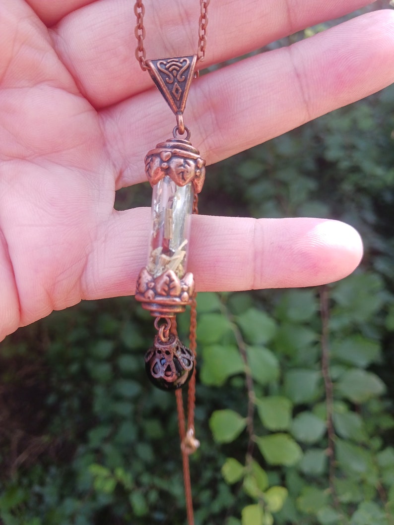 May include: A copper necklace with a long, clear glass pendant filled with dried herbs and a black bead at the bottom.