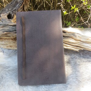 May include: A brown leather-bound journal with a dark brown elastic closure. The journal has a textured surface and a subtle sheen.