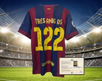 May include: A blue and red soccer jersey with the text "TRES AMIGOS" and the number "122" on the back. The jersey has the signatures of three soccer players. The jersey is displayed in front of a stadium backdrop.