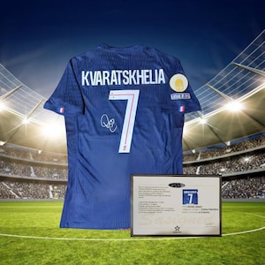 May include: A navy blue football shirt with the name "KVARATSKHELIA" and the number "7" on the back. The shirt has a signature and is displayed with a framed certificate of authenticity. The background shows a stadium.
