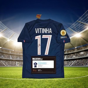 Pode incluir: Uma camisola de futebol azul marinho com o nome "VITINHA" e o número "17" em branco. A camisola tem um emblema da Ligue 1 e uma pequena assinatura. Um certificado emoldurado está anexado.