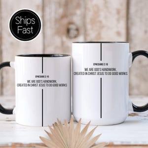 May include: Two white ceramic mugs with black handles and rims. Each mug features the text "Ephesians 2:10" and the quote "We are God's handiwork, created in Christ Jesus to do good works" in black lettering. A "Ships Fast" sticker is visible.
